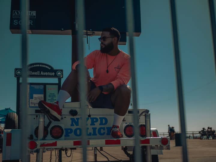 Stylish man in sunglasses poses on an NYPD vehicle at Coney Island boardwalk, NYC.