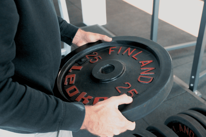 Close-up of a person holding a 25 kg weight plate in a gym.
