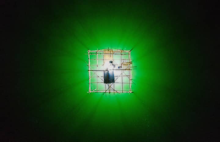 Aerial view of a luminous fishing platform in a vibrant green water setting in West Java, Indonesia.