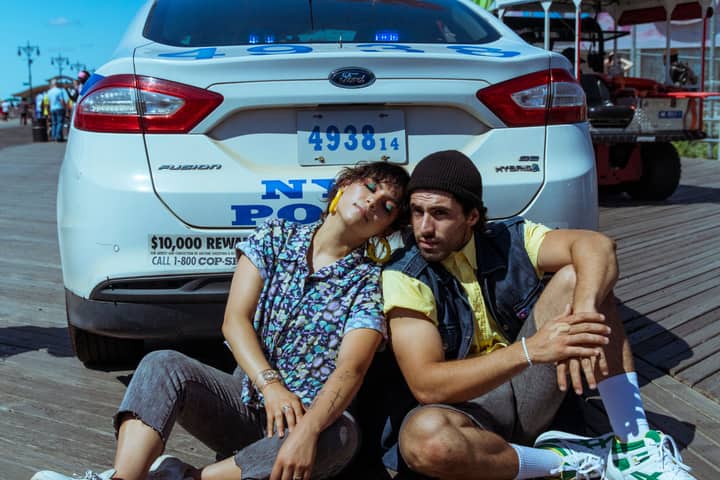 A young couple casually posing by an NYPD car on a sunny day, exuding a relaxed vibe.