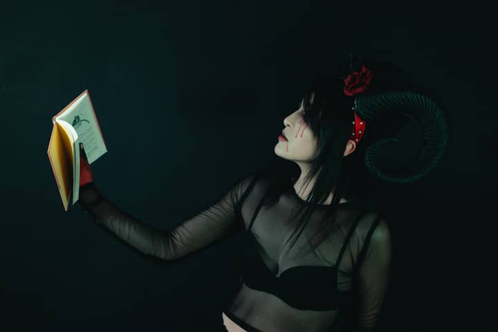 Artistic portrait of a woman in a horned costume holding a book, evoking a dark fantasy theme.