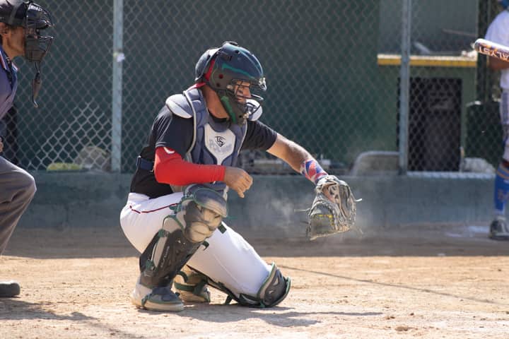 Baseball catcher ready to catch a pitch during a sunny game outdoors.