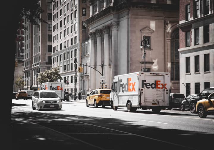 Busy street in New York City with delivery vans and cars in front of historic architecture.