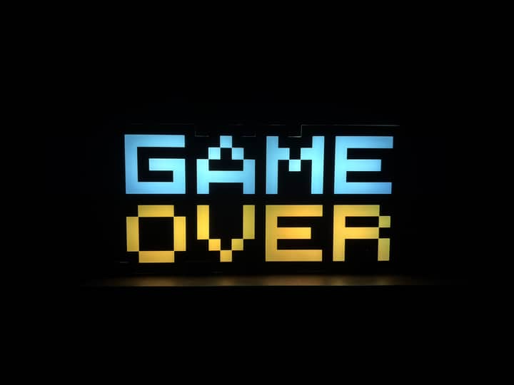 Illuminated pixel art 'Game Over' sign with vibrant colors against a black background.