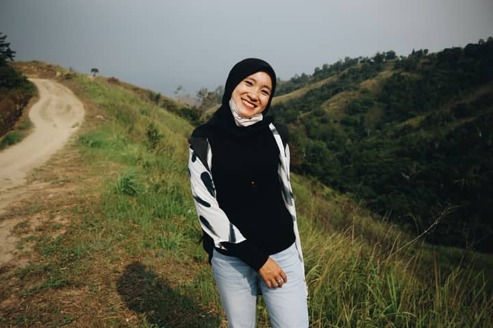 A cheerful woman in casual wear smiling on a scenic mountain path, exuding happiness.