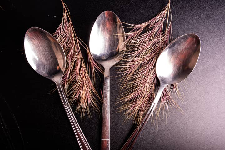 Three metallic spoons creatively arranged with pine leaves on a textured surface.