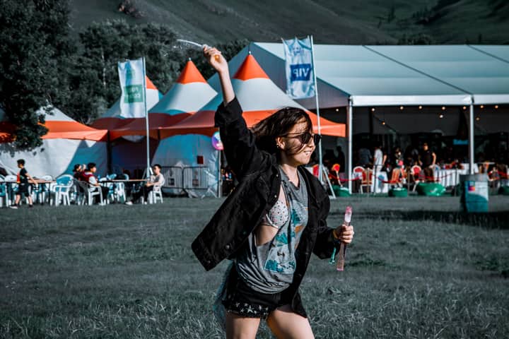 A woman joyfully plays with bubbles at an outdoor festival.