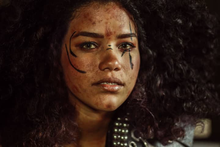 Close-up portrait of a woman with expressive makeup and curly hair in artistic lighting.