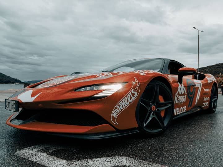 Dynamic shot of an electric sports car adorned with decals on a rainy day in Budva, Montenegro.