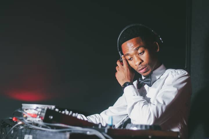 A DJ adjusting headphones while mixing tracks in a dimly lit nightclub scene.