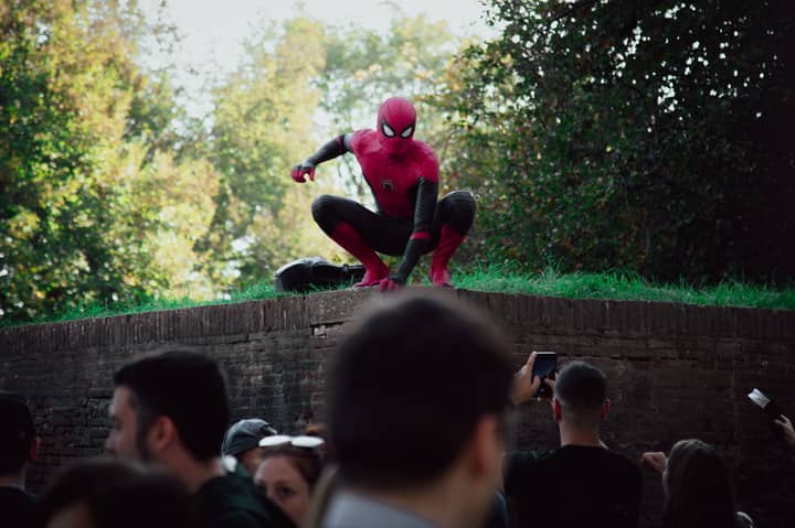 Spider-Man cosplayer posing for photos at an outdoor event, attracting a lively crowd.
