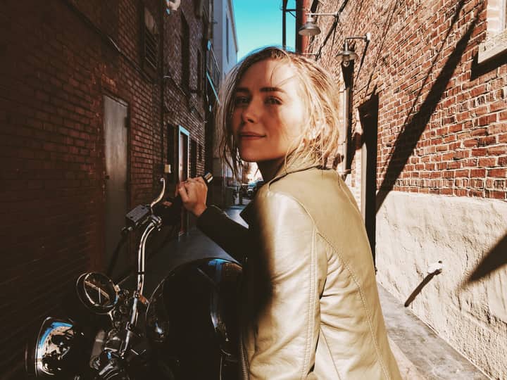 Confident woman in green leather jacket on motorcycle in Atlanta alleyway.