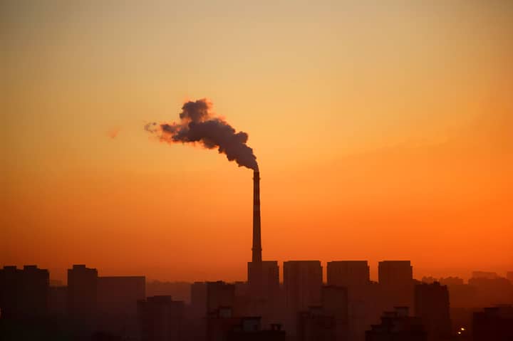 Industrial smokestack emitting smoke during sunset, highlighting environmental impact.