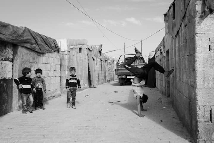 Children play and demonstrate acrobatics in a Syrian refugee camp, showcasing resilience and joy.
