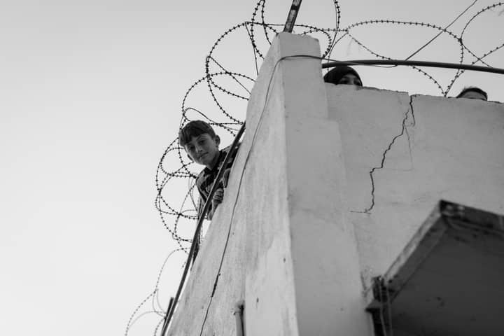 A child looks over a barbed-wire balcony, symbolizing hardship in Lebanon.
