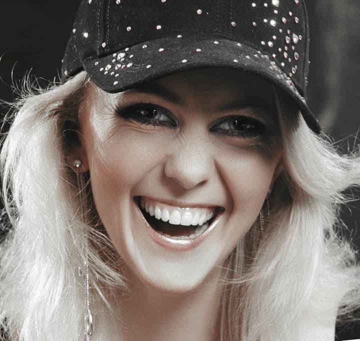 Close-up of a joyful woman with a sparkling cap, laughing vividly indoors.