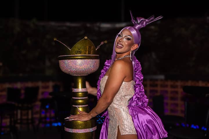 A vibrant performer in a purple outfit poses with a sparkling trophy during a night event.