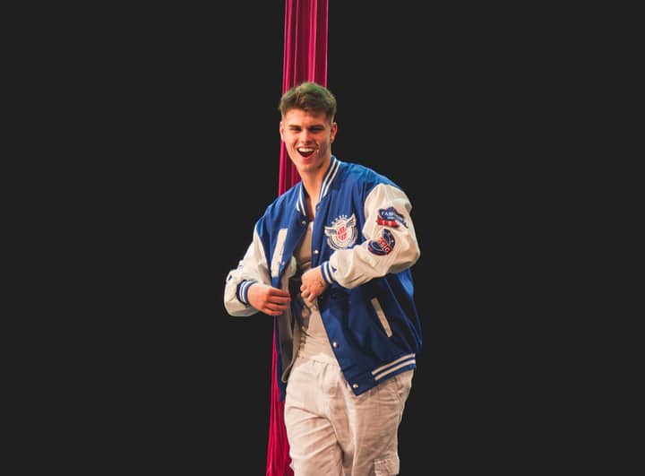 Teenager performing aerial dance in Brazil, wearing a blue jacket against a black background.