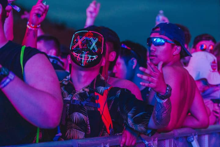 Energetic crowd with neon masks at an outdoor night festival, capturing the lively atmosphere.