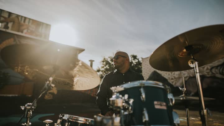 Man playing drums outdoors in San Juan with sunlight creating a dramatic effect.