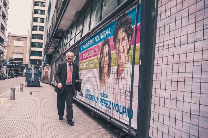 Elderly man walks past colorful political posters in an urban alleyway.
