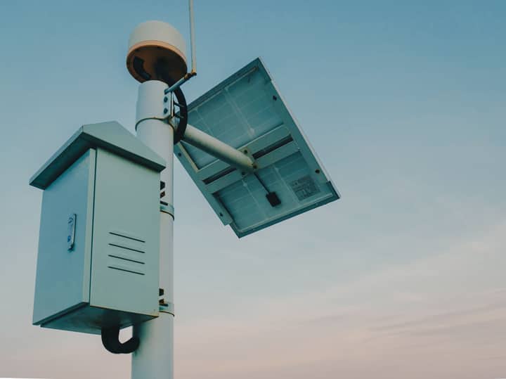 A solar panel paired with a security camera against a clear sky, representing renewable technology.