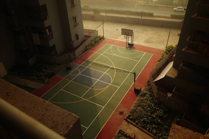 A peaceful urban sports court viewed from above during sunset, showcasing a basketball hoop and tennis lines.