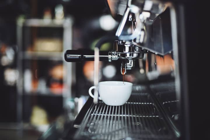 Close-up of espresso machine brewing coffee into a white cup in a cafe setting.