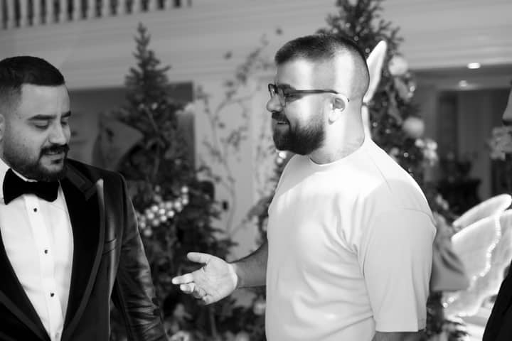 Two men engage in conversation at a formal event decorated for the holidays.