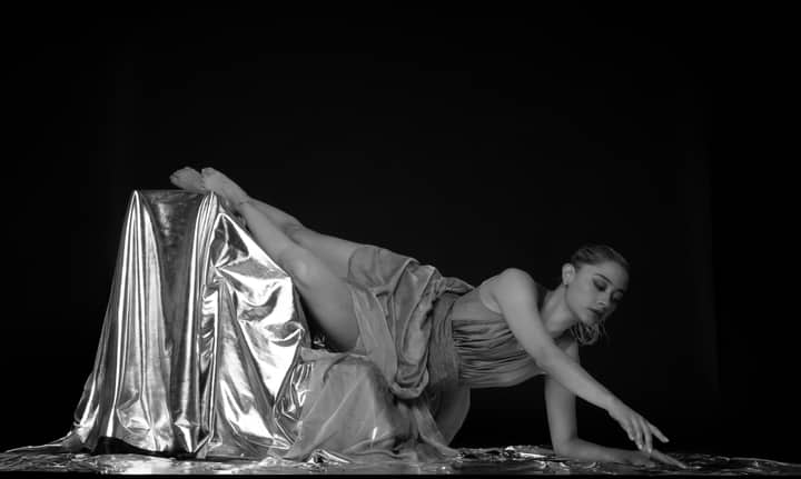 Black and white photo of a graceful ballerina posing with metallic fabric, showcasing elegance and artistry.