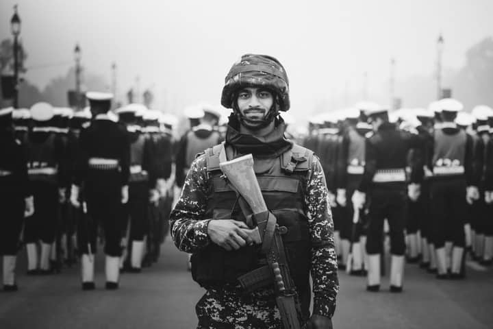 A soldier stands in focus during a military parade in monochrome.