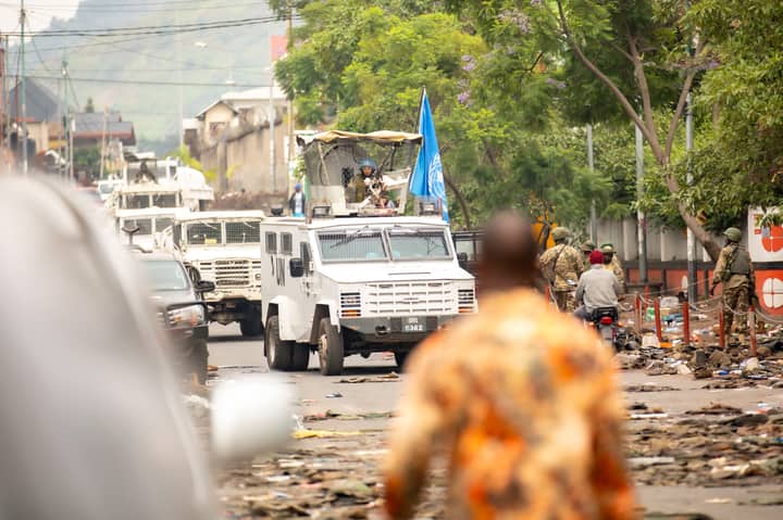 UN armored vehicles and peacekeepers patrol a busy urban street.