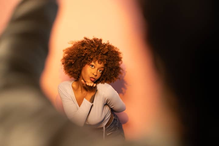 A woman blowing a kiss with dramatic lighting and warm background.
