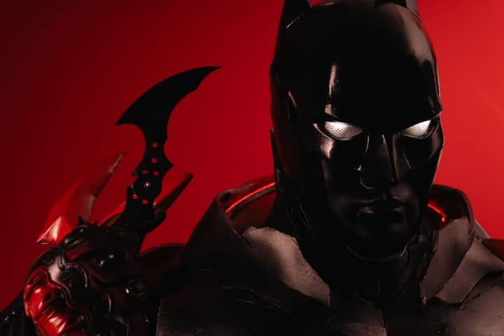 Dramatic portrayal of Batman cosplay against a vivid red backdrop, emphasizing iconic details.