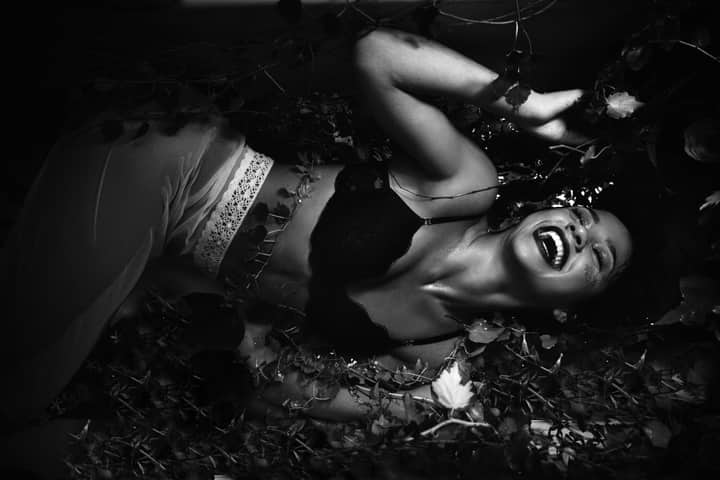 Black and white portrait of a smiling woman surrounded by leaves, conveying joy.