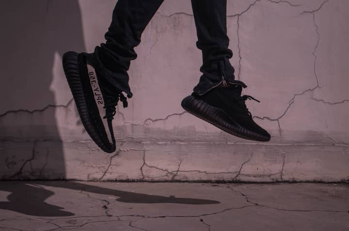 A stylish and dynamic urban photo capturing black sneakers in mid-jump against a cracked concrete wall.