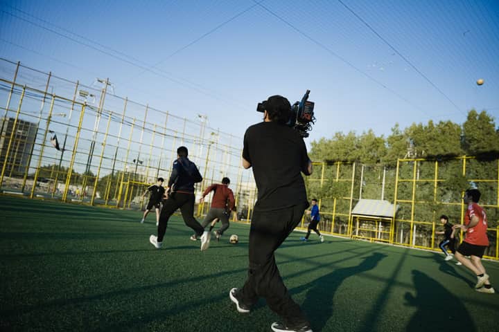 Dynamic scene capturing a filmmaker shooting an outdoor soccer match on a sunny day.