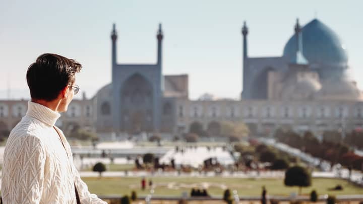 A man gazing at the iconic Sheikh Lotfollah Mosque in Isfahan, Iran, during a sunny day.