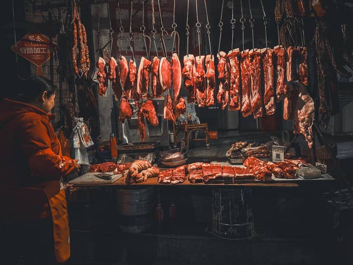 A bustling street meat market stall with hanging cuts of meat and a vendor, captured at night.