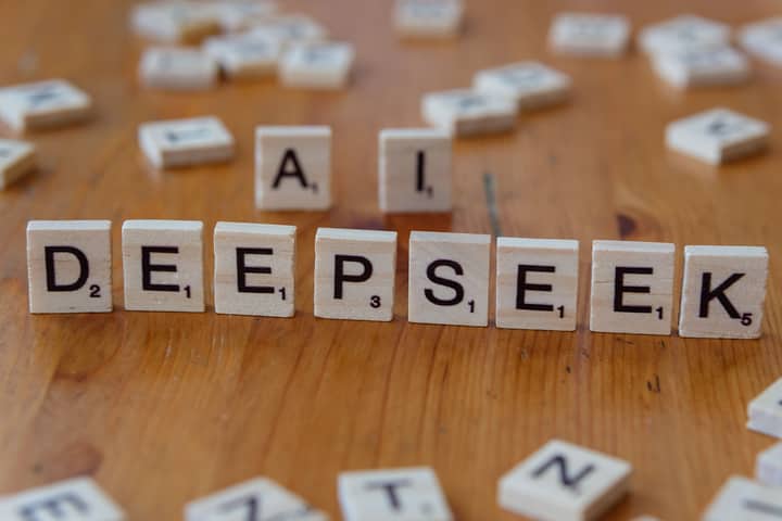 Wooden Scrabble tiles spelling 'DEEPSEEK' with 'AI' on a wooden table, illustrating AI concepts creatively.