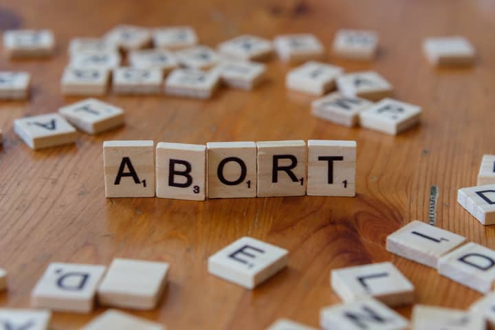 Scrabble tiles spell the word 'abort' on a wooden table, sparking discussion.