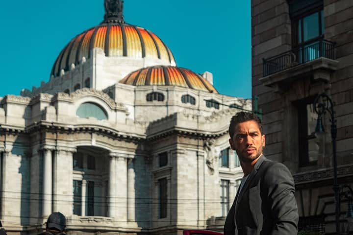 Man standing in front of Palacio de Bellas Artes, Mexico City, under a clear blue sky.