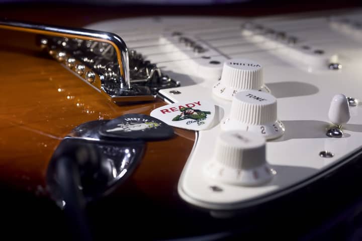 Detailed view of electric guitar showing control knobs, picks, and bridge in focus.