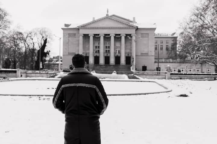 Man standing before Poznań Opera House in winter, showcasing architecture amidst snowy surroundings.