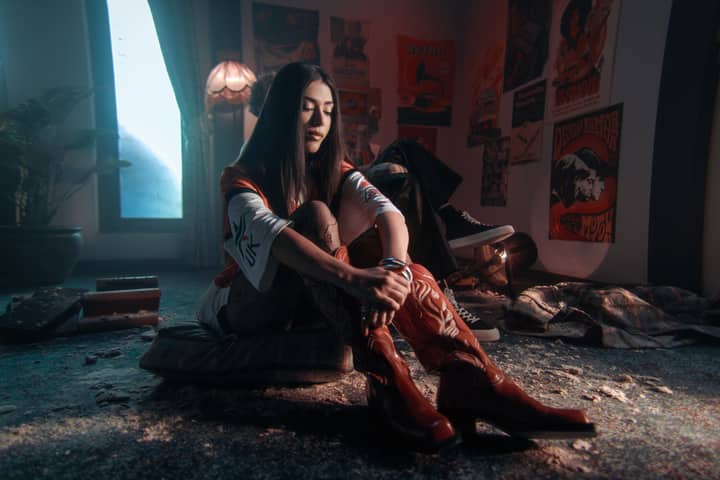 Woman sitting on floor in retro-style room with posters and dim lighting, reflecting nostalgia.