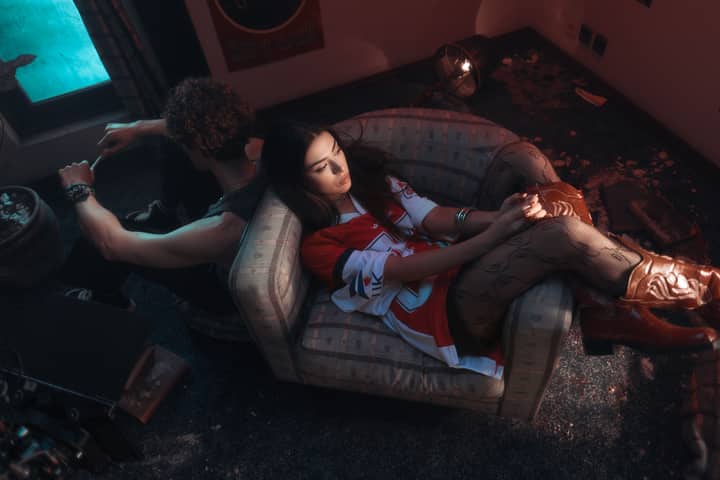 Two young adults in a moody room, both sitting back to back, one on a couch.