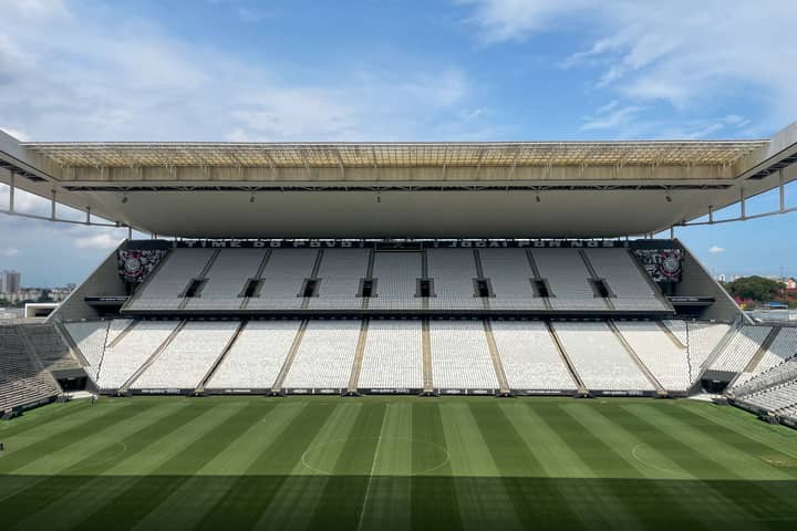 Wide view of an empty football arena in São Paulo, featuring a green pitch under a sunny sky.