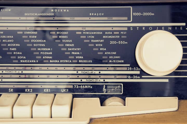 A detailed view of a vintage radio's tuning dial with city stations displayed.