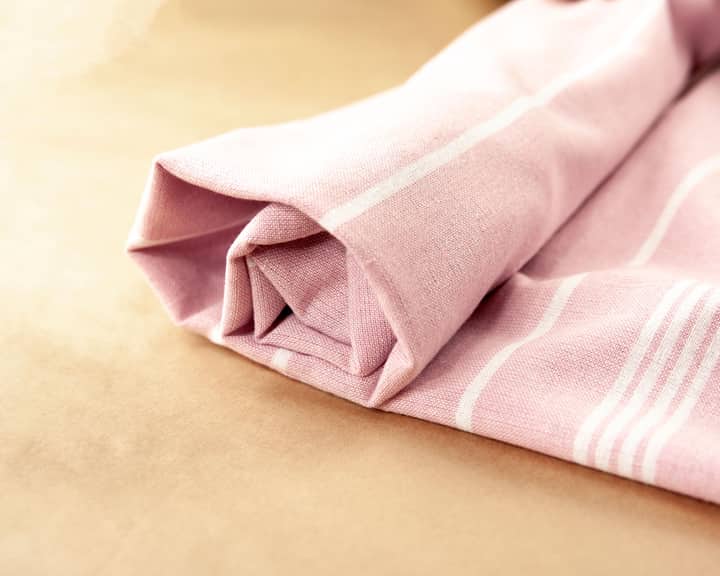 Close-up of a folded pink striped towel on a beige background, highlighting soft textures.
