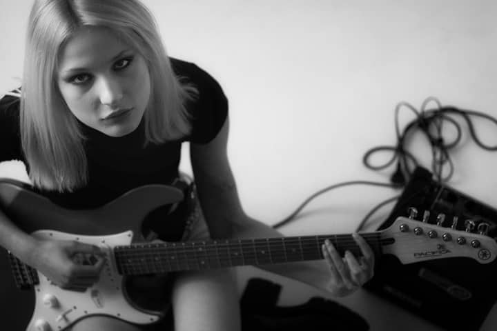 Black and white portrait of a woman playing an electric guitar, showing emotion.